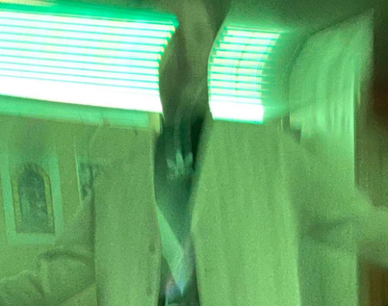 Distorted figure stands in neon lit room.
